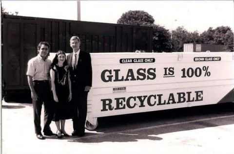 Photo taken in 1990 of 1 woman and 2 men standing in front of a glass recycling receptacle