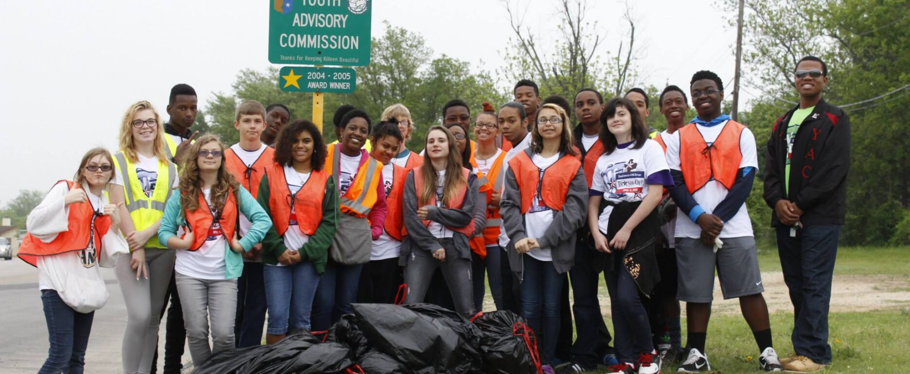 Group poses next to a adopt a highway sign for a Fall Sweep event